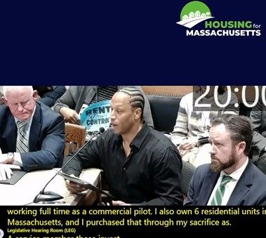 The photo includes three men sitting at a table. The man in the middle is speaking. He is wearing a black button down shirt.